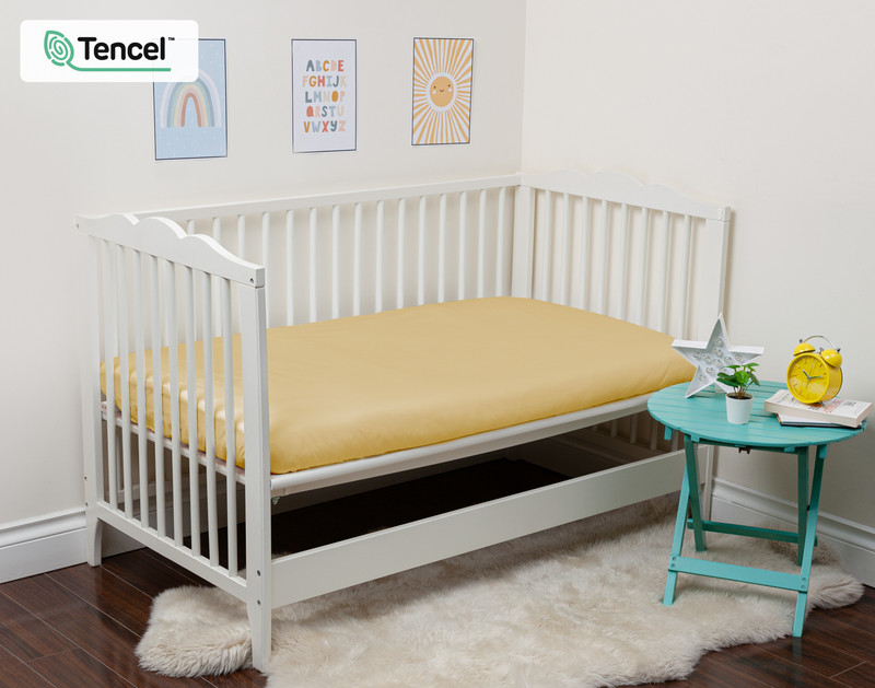 Our BeechBliss Crib-Sized Fitted Sheet in Sun Shower dressed over a small mattress in an open crib.