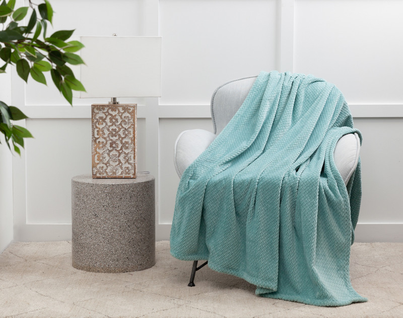 Our Chevron Plush Throw in Aqua over a white chair next to an lamp table.