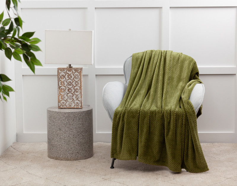 Our Chevron Plush Throw in Moss over a white chair next to an lamp table.