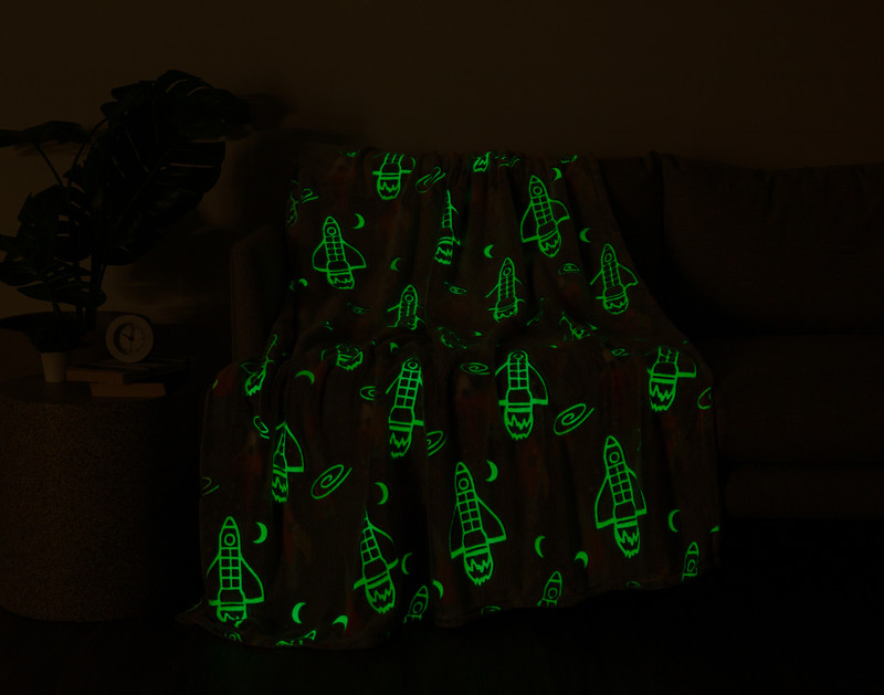 Our Rocket Glow in the Dark Fleece Throw sitting with a light green glow in a darkened living room.