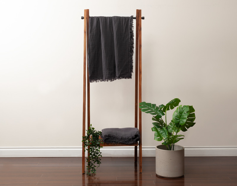 Front view of our Muslin Gauze Throw in Obsidian hanging on a tall fixture next to a short leafy plant.