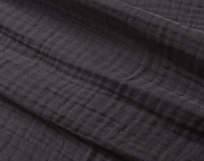 Close-up on our Muslin Gauze Throw in Obsidian to show its subtle grid-like texture and cozy cotton and lyocell surface.