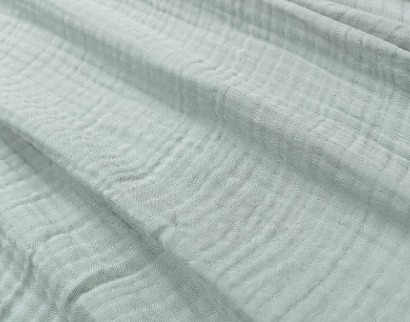 Close-up on our Muslin Gauze Throw in Seagrass to show its subtle grid-like texture and cozy cotton and lyocell surface.