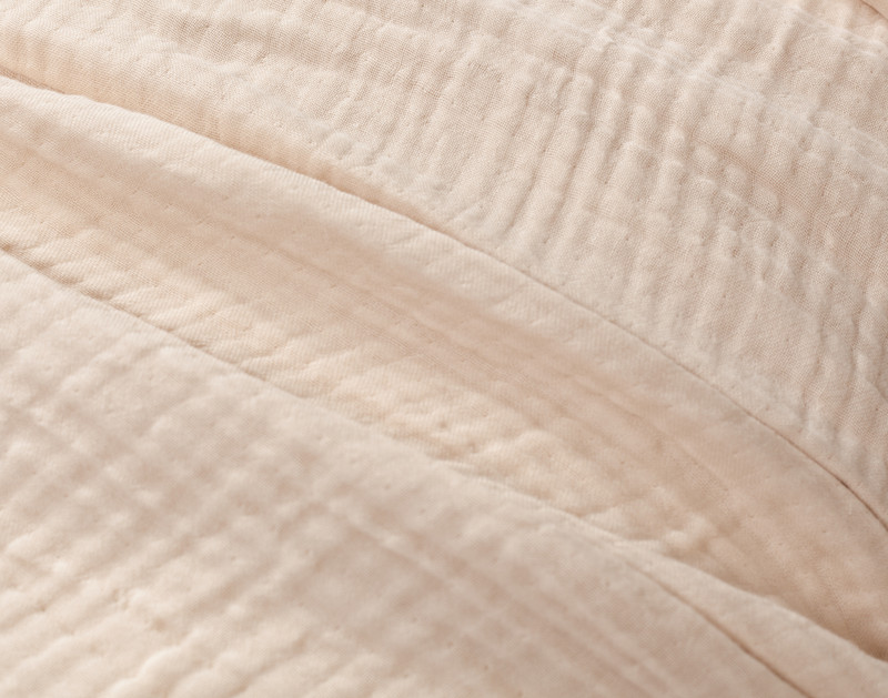 Close-up on our Muslin Gauze Throw in Natural to show its subtle grid-like texture and cozy cotton and lyocell surface.