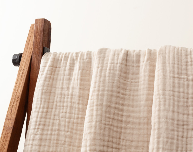 Close-up of our Natural Muslin Gauze Blanket hanging from a fixture to show its natural drape.