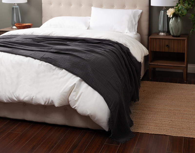 Angled view of our Obsidian Muslin Gauze Blanket thrown over a white queen bed.