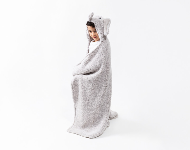 Side view of a school-aged child wrapped up in our Elephant Hooded Animal Throw in a plain white room.