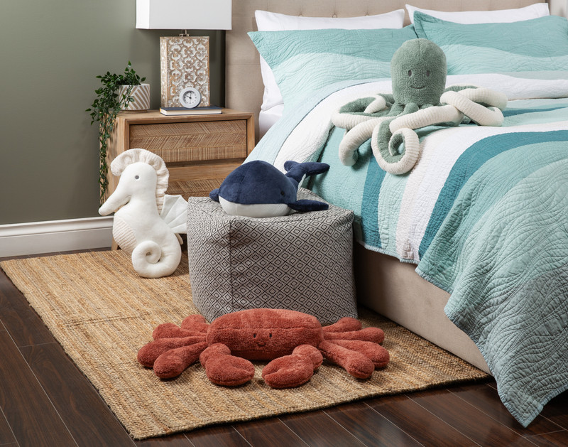 Angled low view of all four of our Sea Animal Cushions sitting next to watery blue bed and beach-inspired wood and wicker décor.