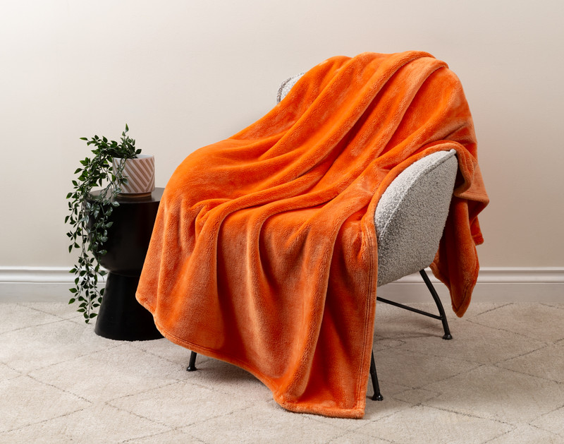 Our Velvet Plush Throw in Sundown draped over a beige chair in a white living room.