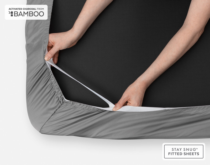 Close-up of two hands stretching our Deep Charcoal Bamboo Cotton Fitted Sheet to show the resilience of its stay snug strap.