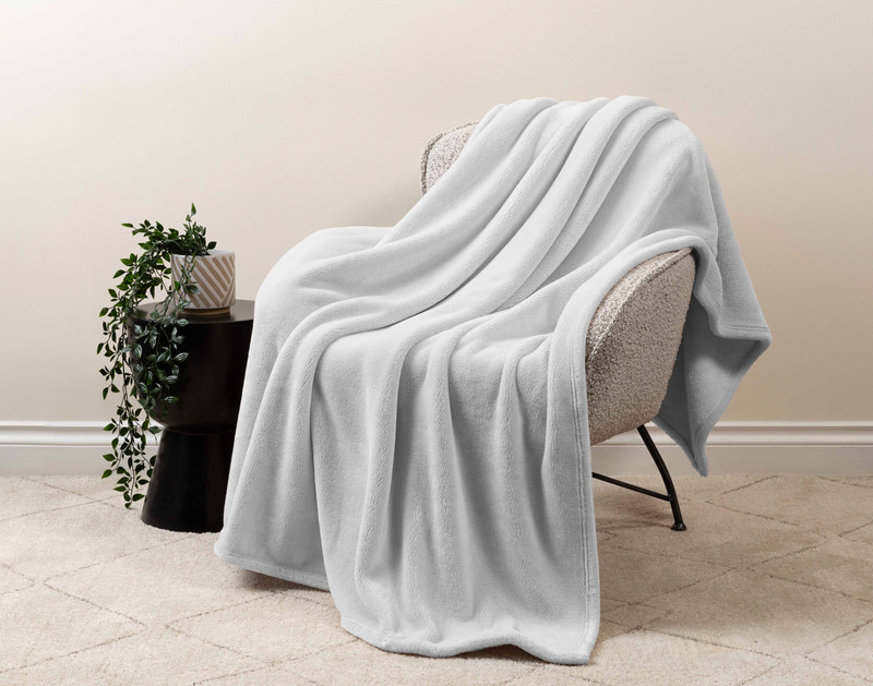 Our Velveteen Throw in Silver draped over a beige chair in a white living room.