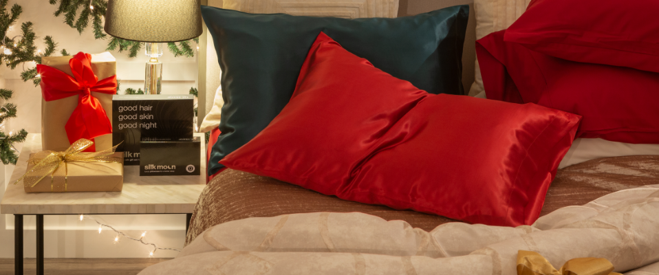 Nos taies d'oreiller Silk Moon stylisées sur un lit à côté d'une pile de cadeaux comprenant nos accessoires Silk Moon pour le Noël 2022.