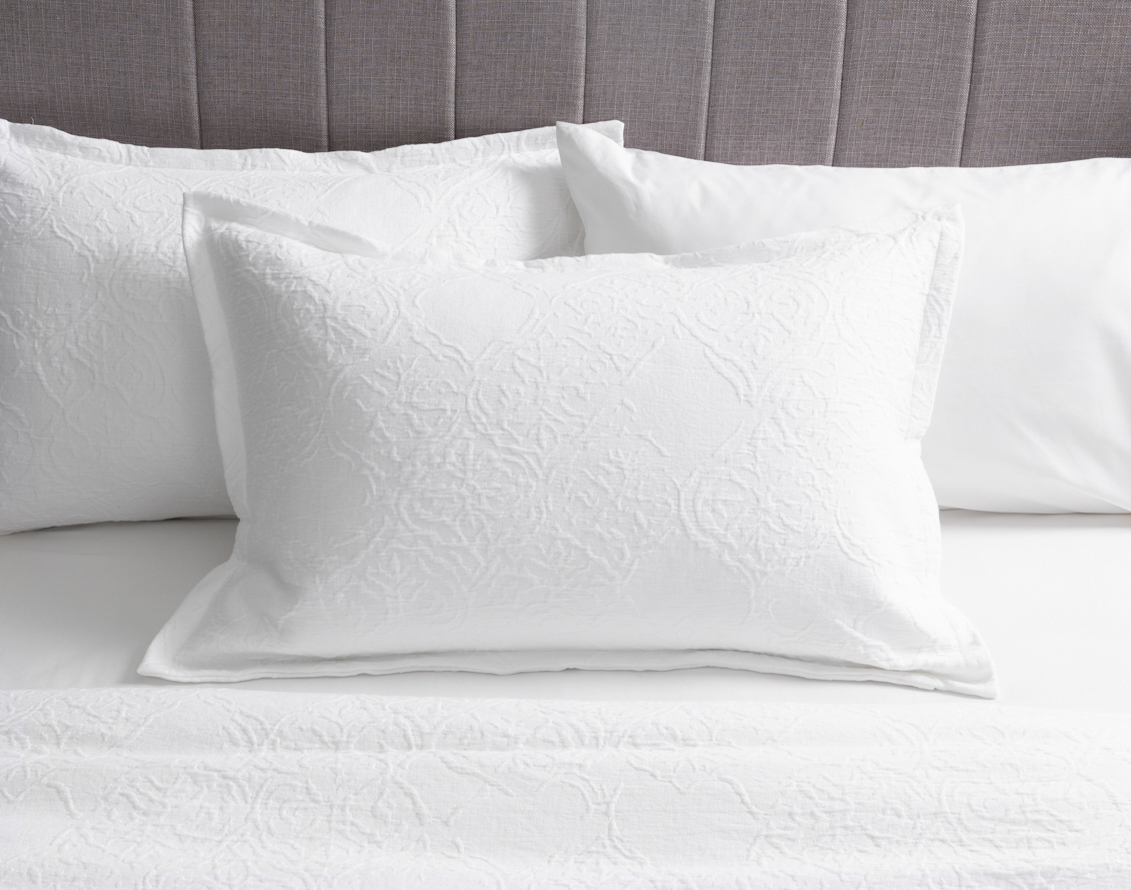 Front view of our Corinthia Pillow Sham sitting over a solid white bed with coordinating pillow shams.