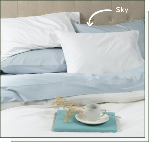 Our Sky Blue Bamboo Cotton Sheet Sets spread over a bed, with a blue book and tea cup.