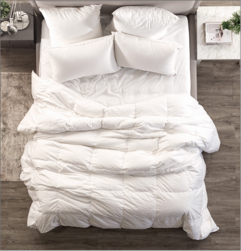 Overhead view of a white bed over a hardwood floor, with a duvet layed flat over top without a duvet cover.