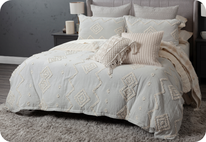 Duvet cover in soft blue-grey with a fringed geometric pattern dressing a queen bed with matching pillow shams and complementary boho-style cushions and a throw.
