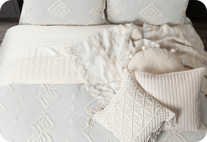 View from above of a duvet cover in soft blue-grey with a fringed geometric pattern dressing a queen bed with matching pillow shams and complementary boho-style cushions and a throw.