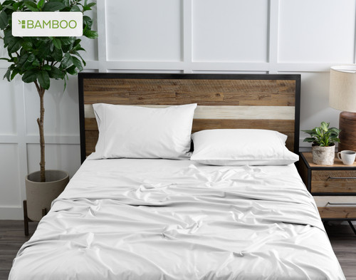 Top view of our Bamboo Cotton Sheet Set in White dressed over a wooden bed in a white plant-filled bedroom.