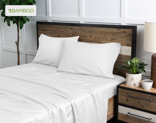 Angled view of our Bamboo Cotton Sheet Set in White dressed over a wooden bed in a white plant-filled bedroom.