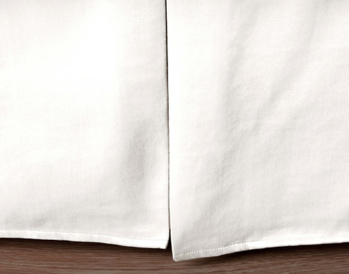 Close-up of our Blanchard White Bedskirt hanging over a hardwood floor.