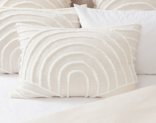 Front view of our Sonrisa Pillow Sham sitting in front of multiple coordinating pillows on a white bed.