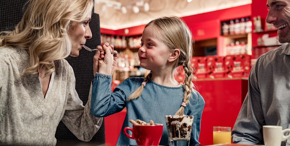 Little girl feeds her mom chocolate desert on a spoon.