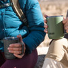 Two CamelBak Horizon Vacuum Camp Mugs in dark grey and olive green, held by individuals seated outdoors.