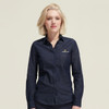 A woman wearing a navy denim button-up shirt with a logo on the chest pocket.