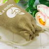 A small jute gift bag in beige with a drawstring closure, featuring a logo, placed among flowers.