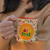 A coffee mug with a vibrant orange interior and a multicoloured fruit-themed exterior, featuring a logo.