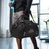 A black sports bag with a shoulder strap, being held by a person, featuring a logo and a drink bottle attached.