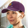 A cap with a white trim and a logo, featuring a purple design. The model is wearing earphones.