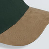 A green cap featuring a suede tan peak, showcasing detailed stitching along the brim.