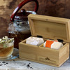 A bamboo tea box with compartments containing assorted tea bags, beside a glass of tea and a teapot.