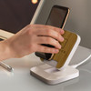 A wireless charging stand with a bamboo top and a white base, featuring a hand placing a phone on it.