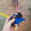 A compact black pet bag dispenser with colourful designs, holding a blue waste bag, and a dog visible in the background.