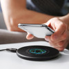 A sleek black wireless charger with a logo, positioned on a table near a smartphone.