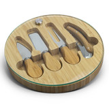 A bamboo cheese board with a glass top, featuring four stainless steel cheese knives fitted in circular compartments.