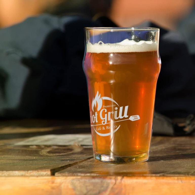 A beer glass filled with amber beer, featuring a logo, sits on a wooden surface.