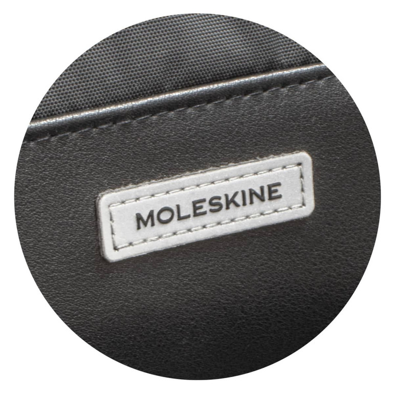 A close-up of a black Moleskine Metro Slim Backpack featuring a white logo tag.