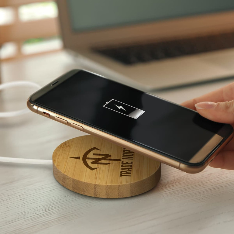 A bamboo wireless charger with a smartphone being placed on it, featuring a charging indicator on the phone's screen.