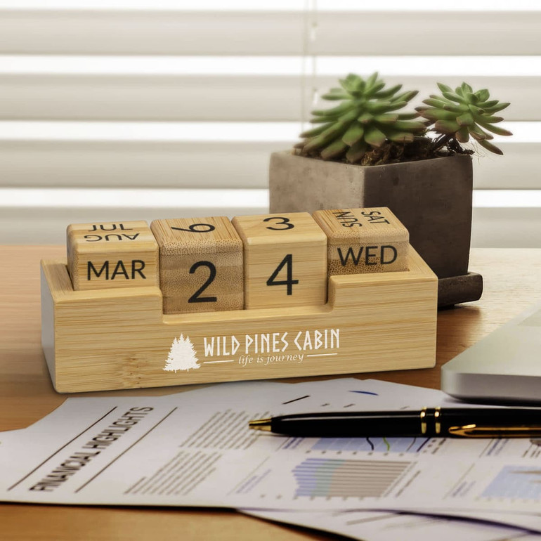 A bamboo desk calendar with wooden blocks displaying the day, date, and month, alongside a small succulent plant.