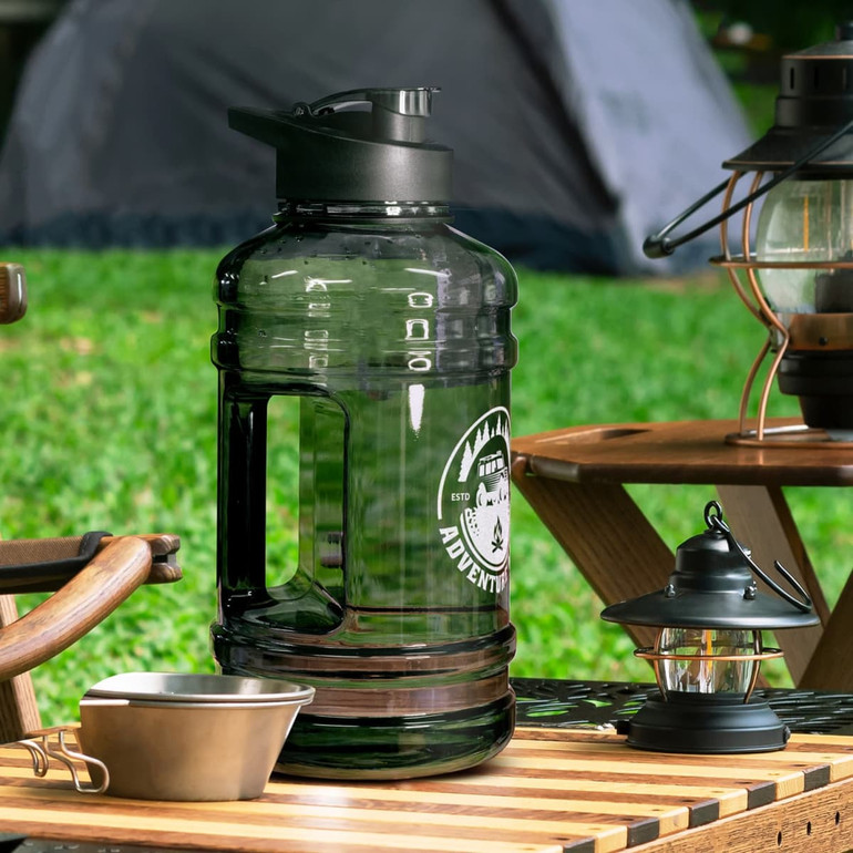 A drink bottle in transparent black with a sturdy handle, placed on a wooden table outdoors.