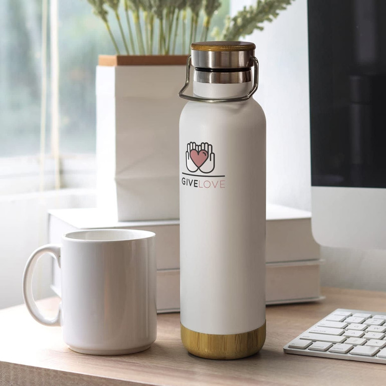 A drink bottle in white with a bamboo base, featuring a logo. A white mug and keyboard are in the background.