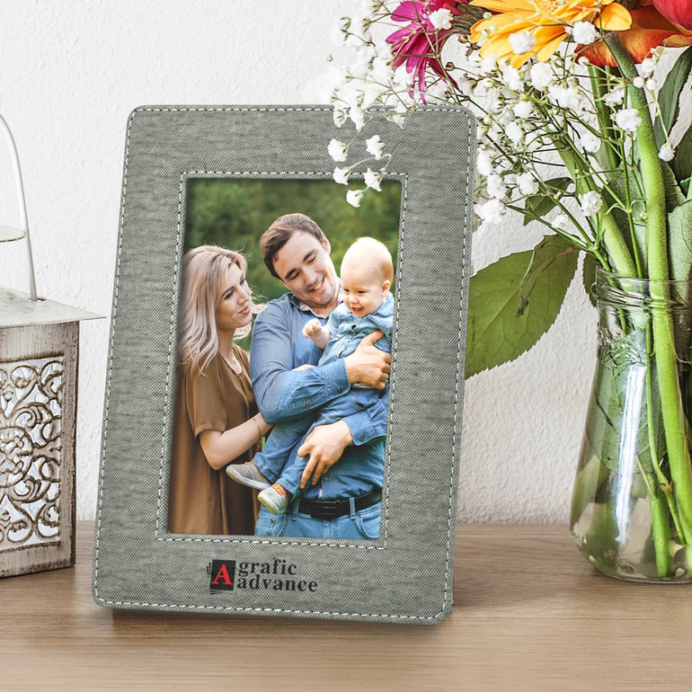 A grey photo frame with a fabric texture, displaying a family photo, beside a vase of flowers and decorative lantern.