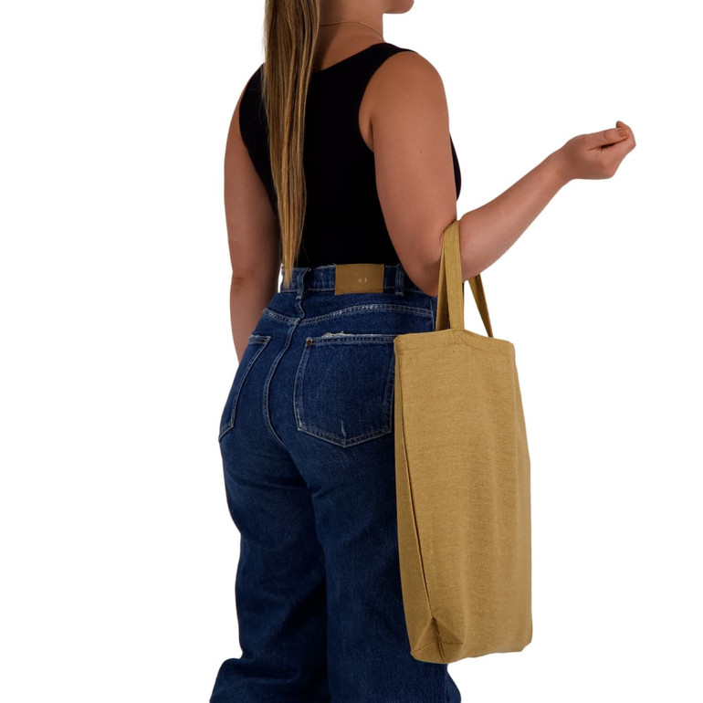 A woman holds a mustard yellow eco-friendly shopping bag with short handles, wearing a black top and blue jeans.