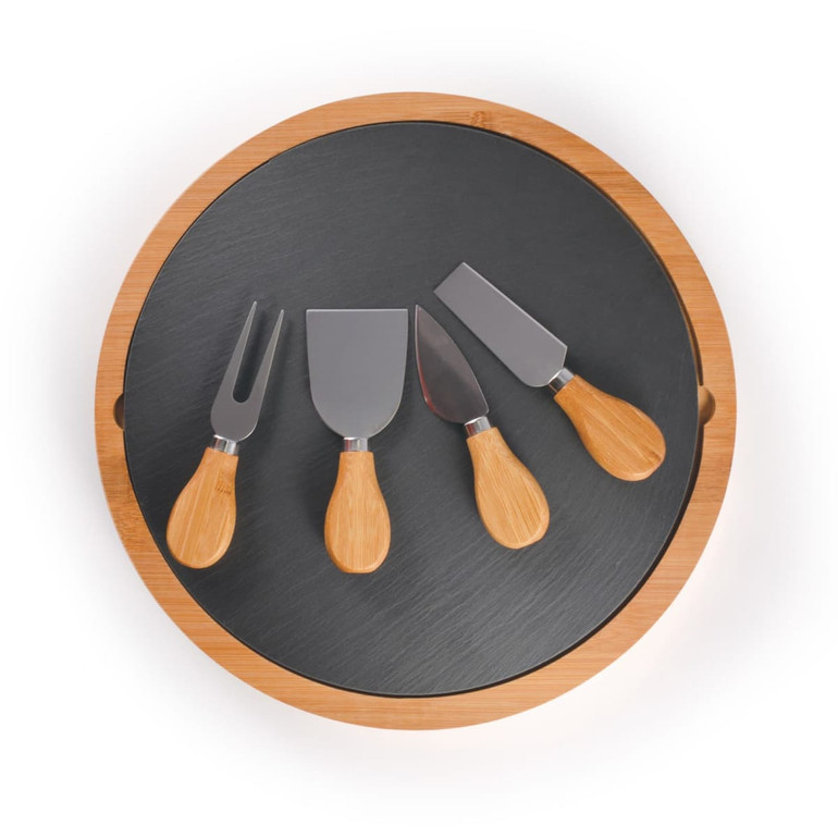 A round bamboo cheese board with a slate surface and four metal cheese knives with bamboo handles.