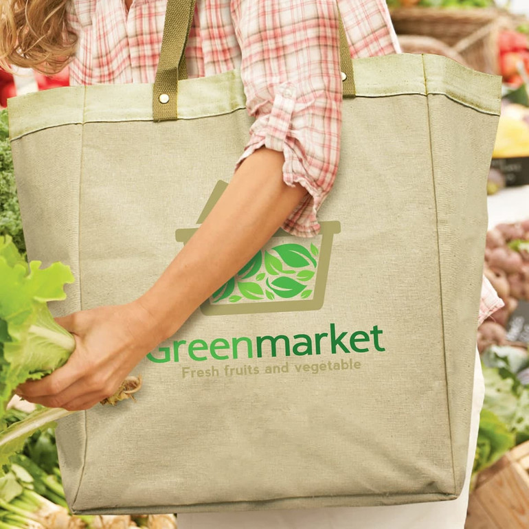 A green tote bag with a logo, held by a person wearing a checked shirt, amidst fresh produce.