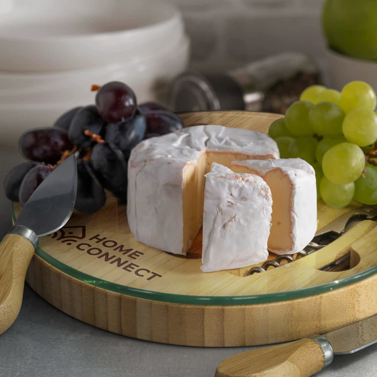 A bamboo cheese board featuring a round cheese, grapes, and a cheese knife, with a logo on the board.