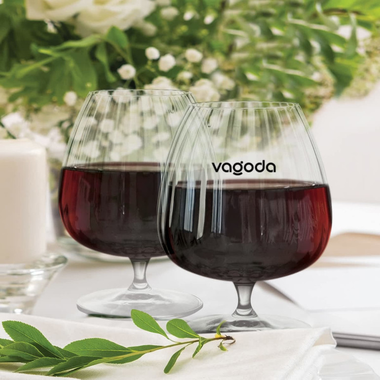 Two transparent cognac glasses with a curved design, filled with dark liquid, set against a floral background.